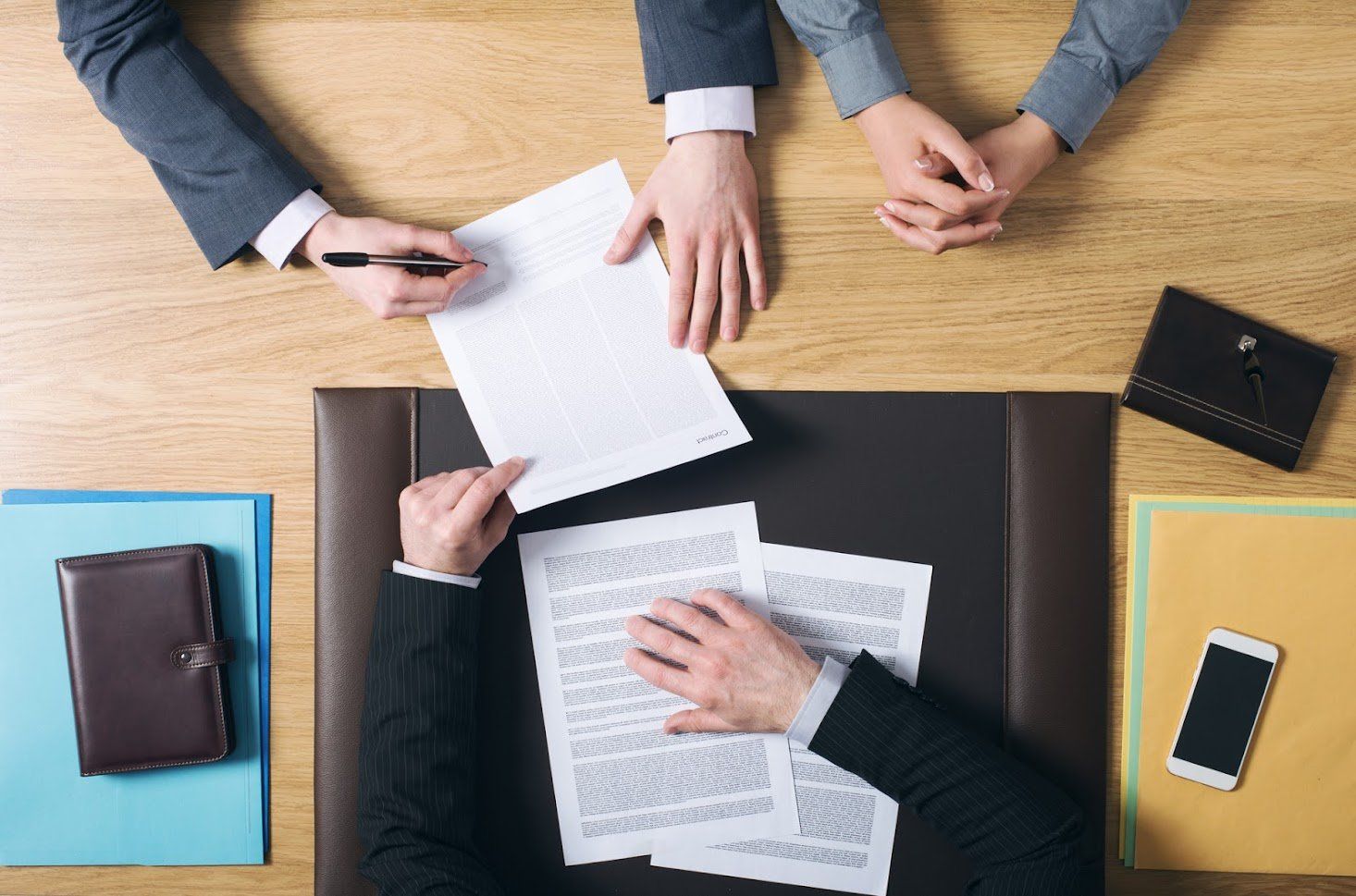 People signing documents at a desk, surrounded by files, a notebook, and a phone.
