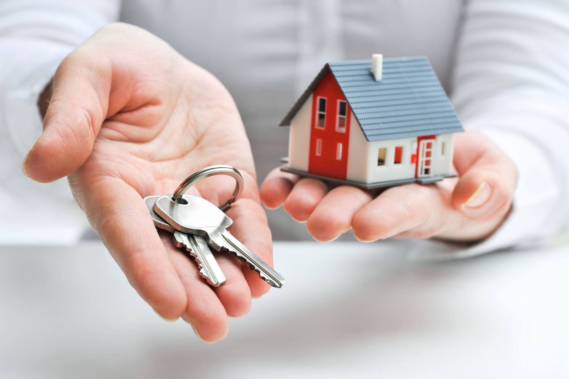 Hands holding house keys and a miniature house, symbolizing home ownership.