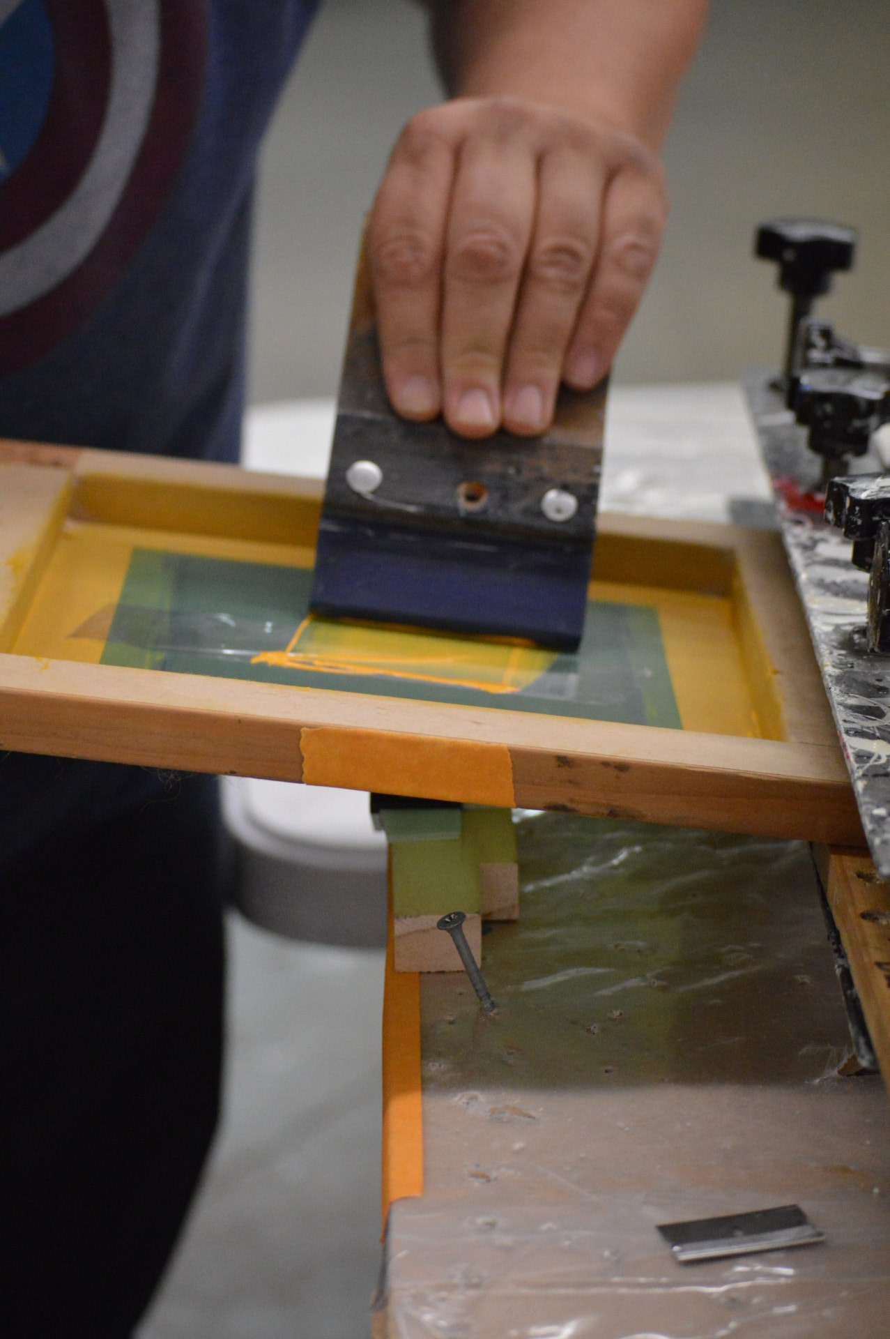 A person is holding a spatula over a screen printing machine.
