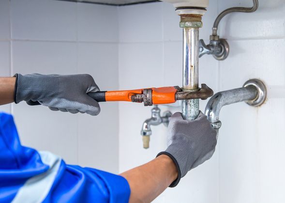 Townsville Plumber using a wrench to repair a water pipe under the sink