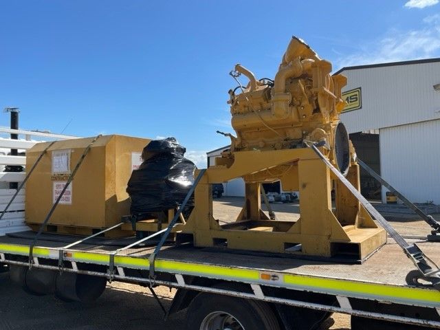 Yellow industrial equipment secured on a flatbed truck against a blue sky.
