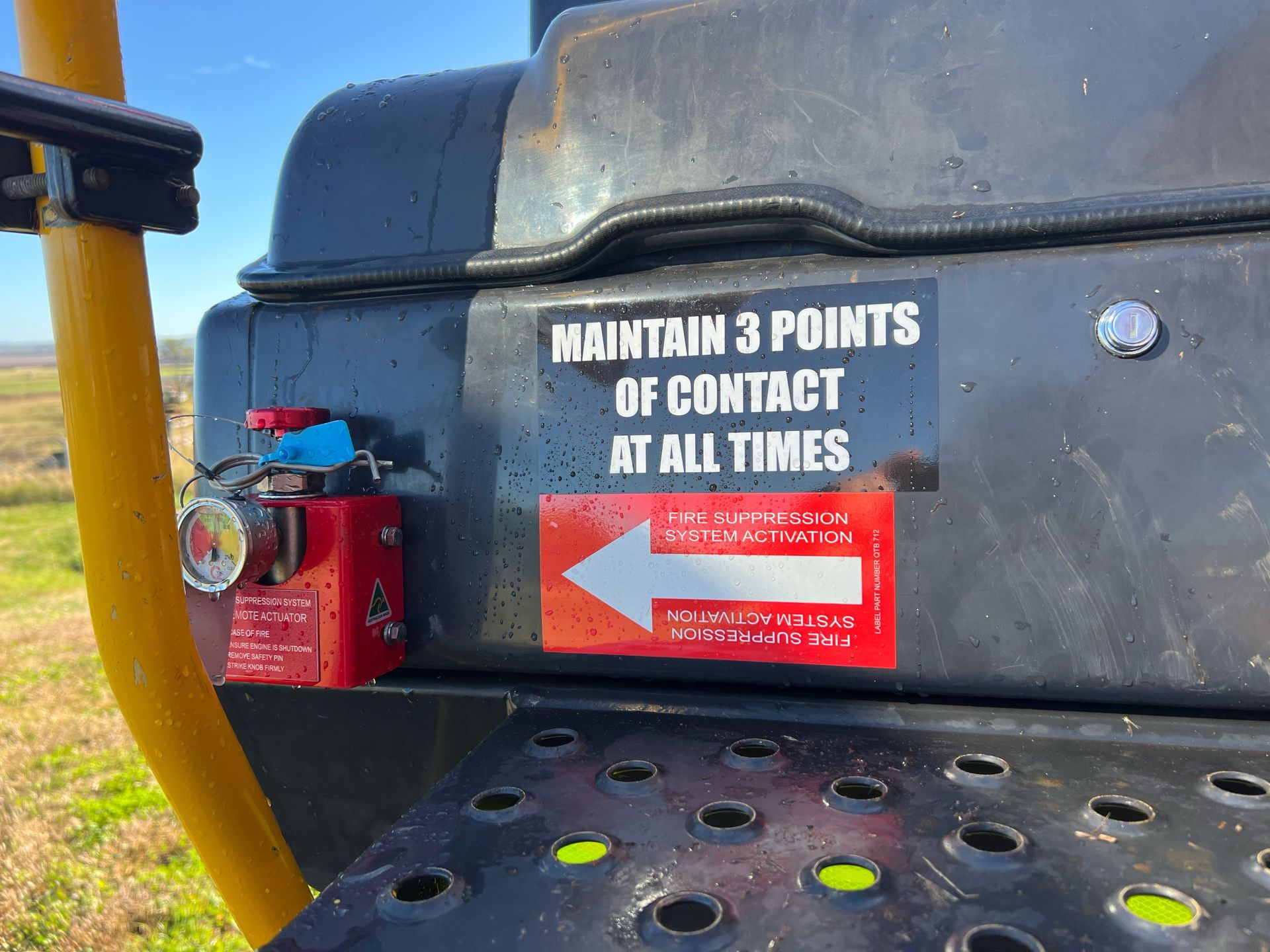 Black machinery with safety signs and a red emergency release, outdoors.