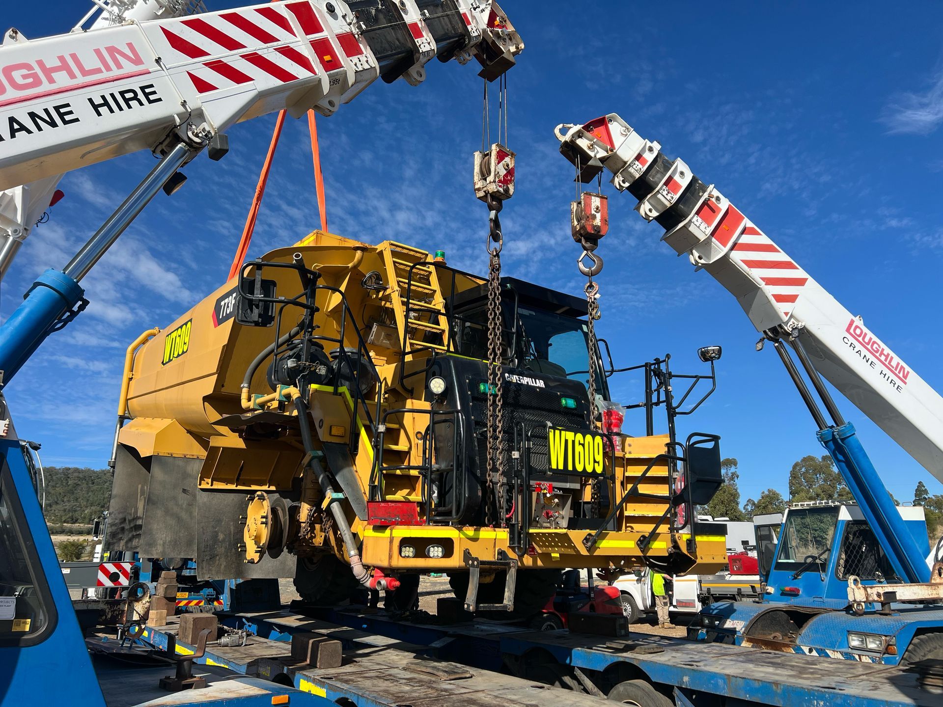 Close-up of machinery, with black motor on top, viewed outdoors with a person and vehicles in the background.