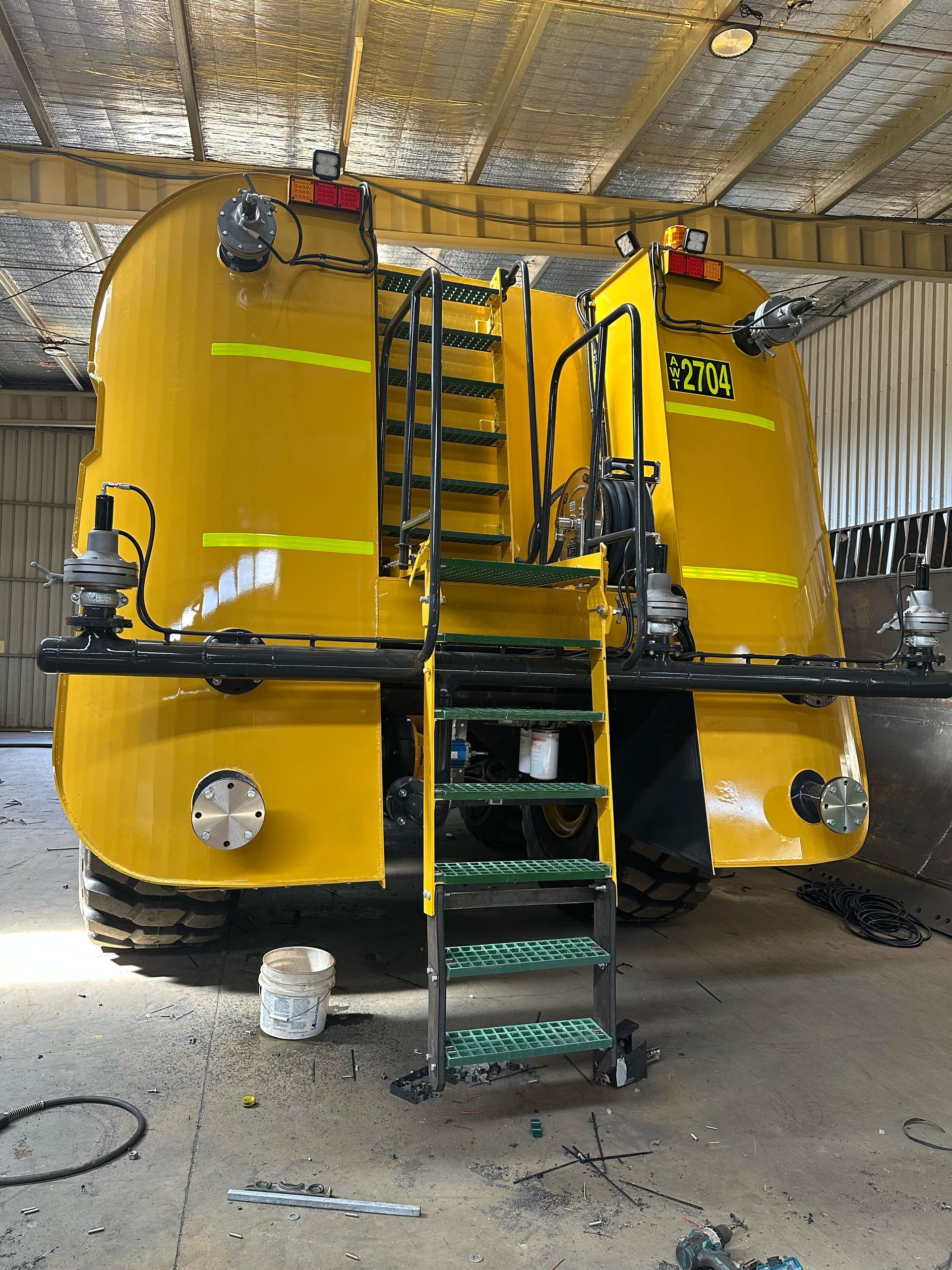 Yellow water tanker with a ladder, parked in a workshop.