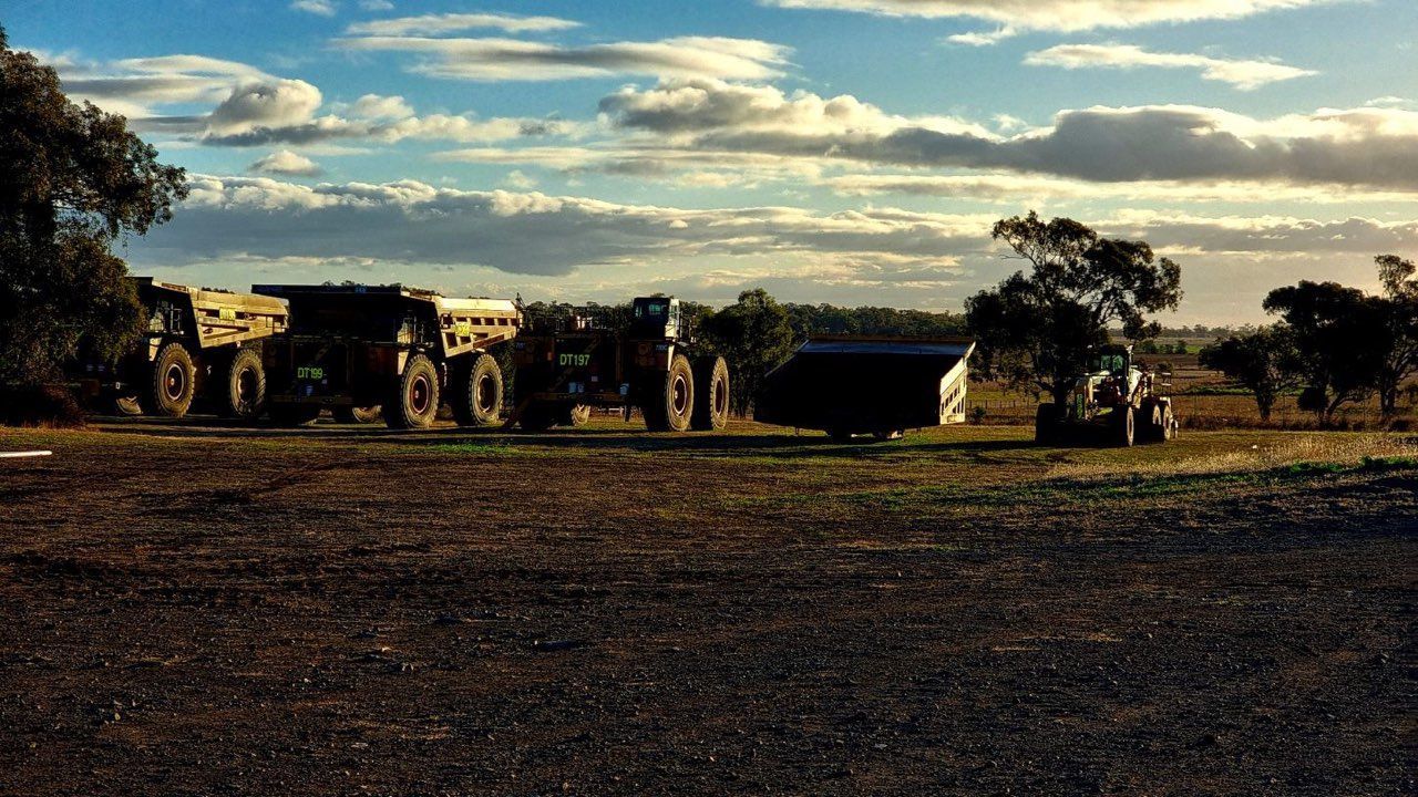 Large mining trucks parked on a dirt lot under a cloudy sky at sunset.