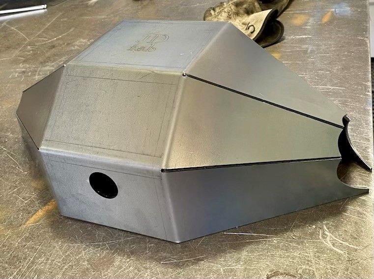 Welded metal box with angular sides, a circular hole, and a work glove in background.