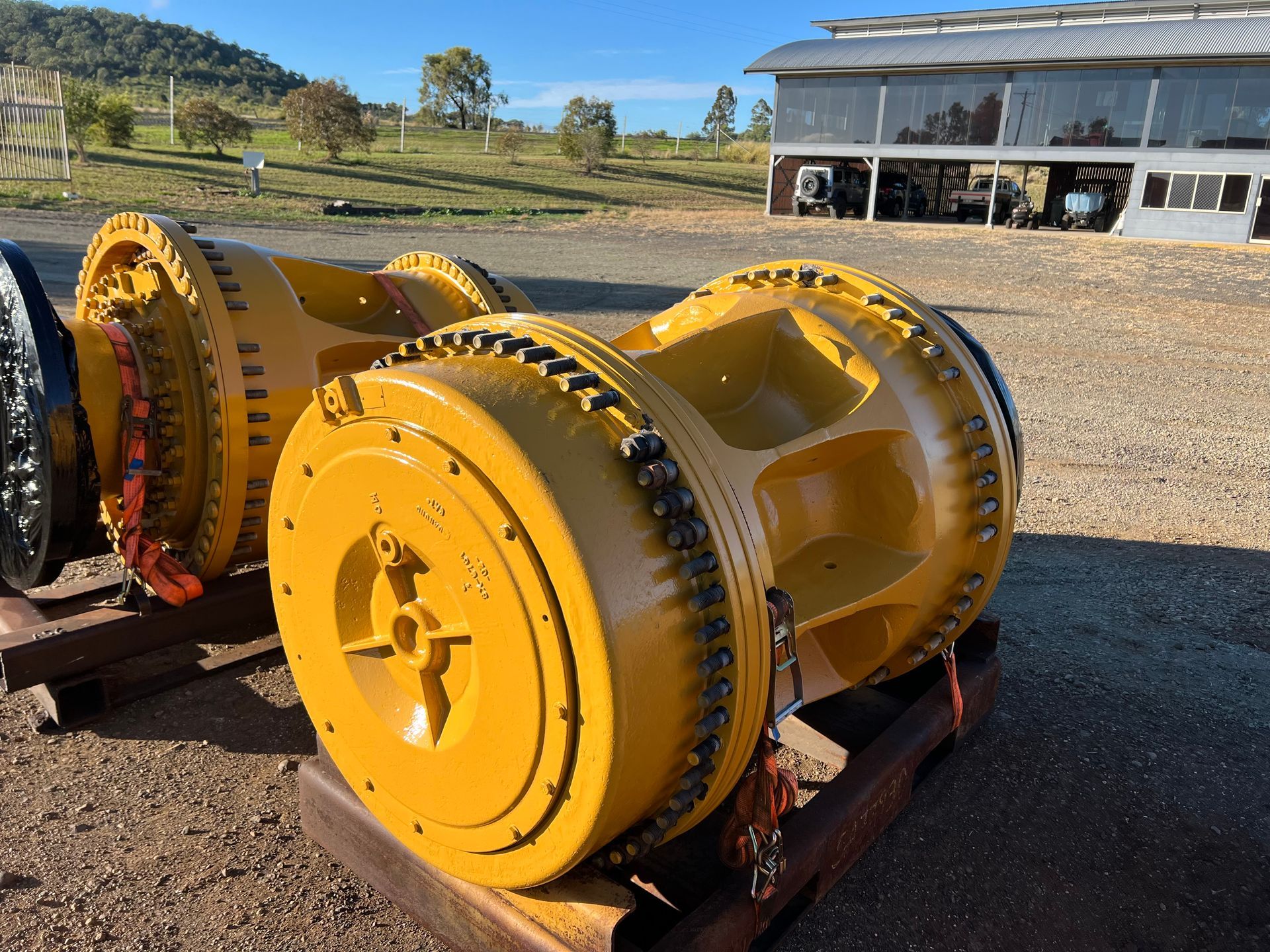Two large yellow industrial wheels outdoors on a wooden pallet. A barn and field are in the background.
