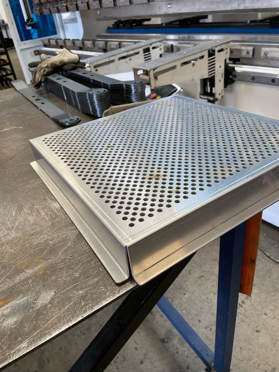 Perforated metal panel with folded edges on a workbench in a workshop.