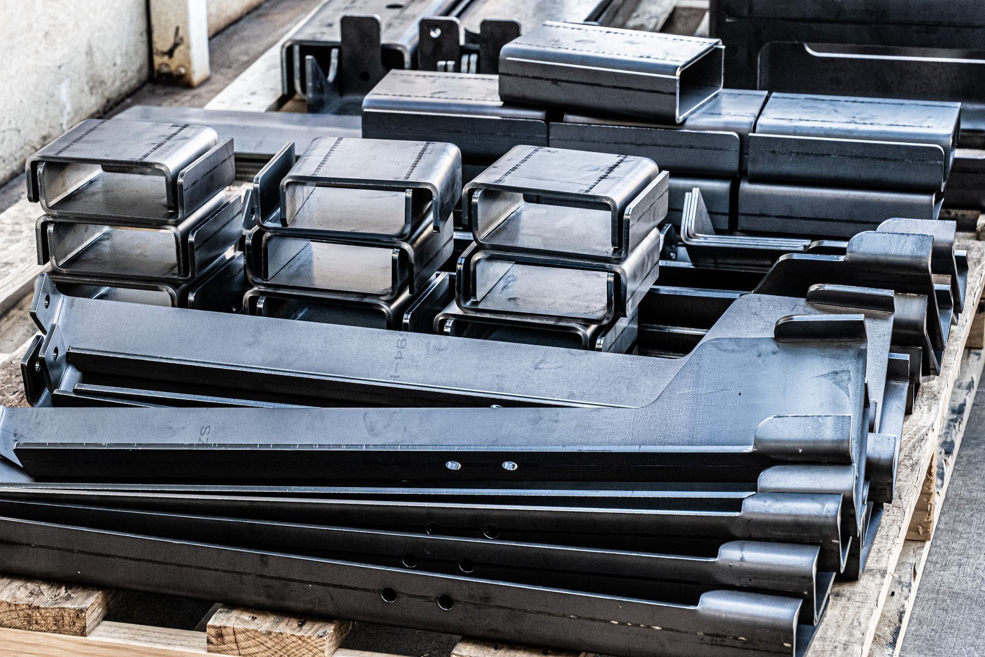 Metal fabricated parts stacked on a wooden pallet in a factory setting.