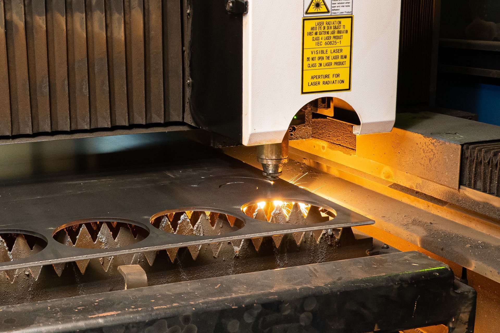 Laser cutter cutting intricate shapes from a metal sheet, sparks and bright light present.