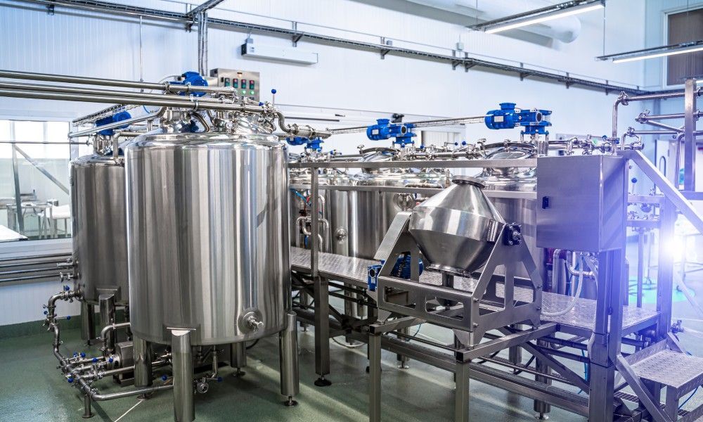 The interior of a food processing plant. There are several stainless steel tanks lined up in rows as