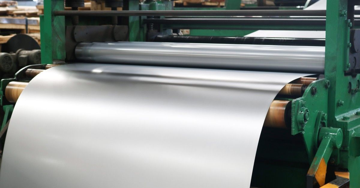 A long stainless steel sheet inside a green plate rolling machine. The stainless steel is shiny and free of imperfections.