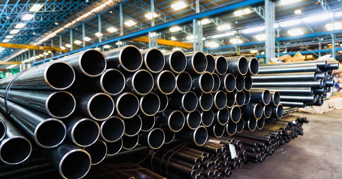 A large quantity of stainless steel pipes stacked on top of one another in a brightly lit warehouse.