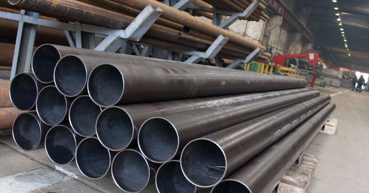 Three rows of steel pipes are stacked on top of wooden blocks on a concrete floor.
