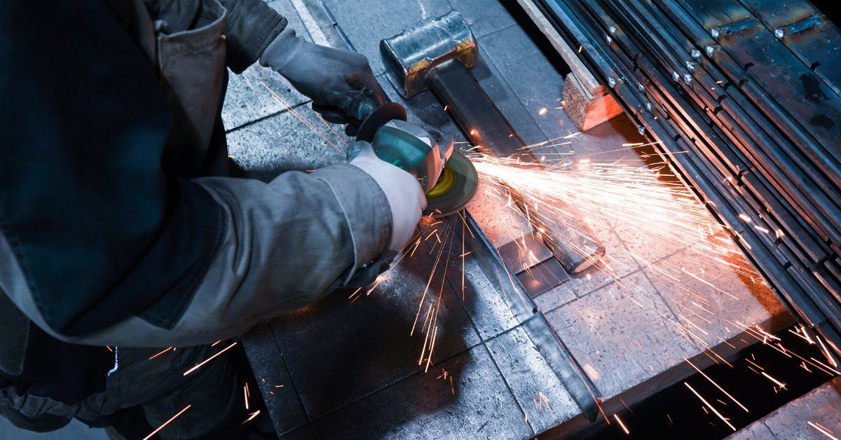 Orange sparks flying as a worker wearing thick gloves and an apron uses a tool to cut through st
