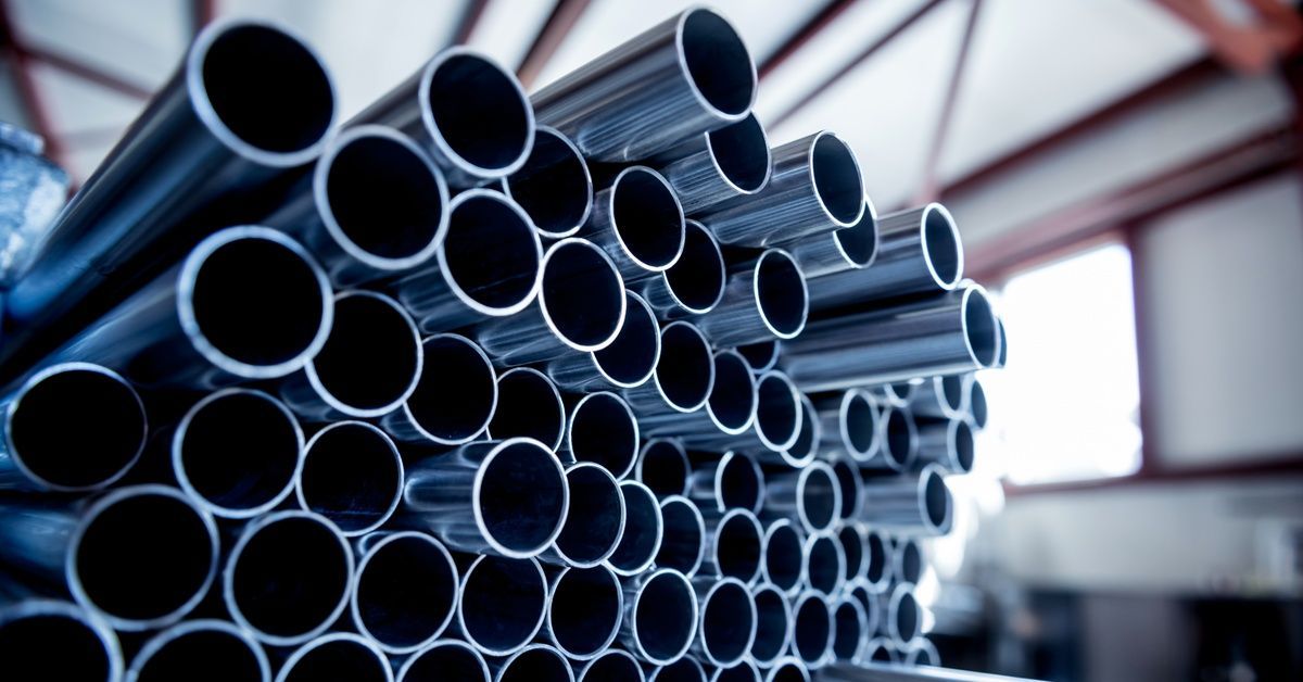 Stainless steel pipes stacked in rows inside a room with red beams on the ceiling.