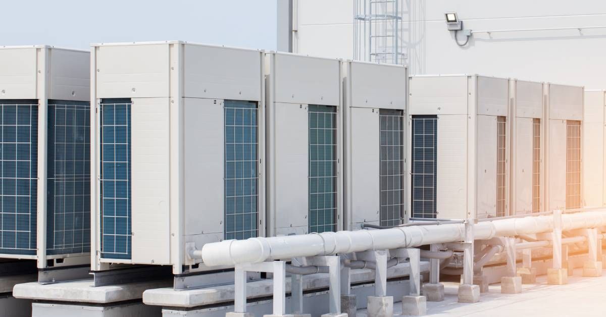 Several white condenser units are being used in central air condition systems lined up on the roof o