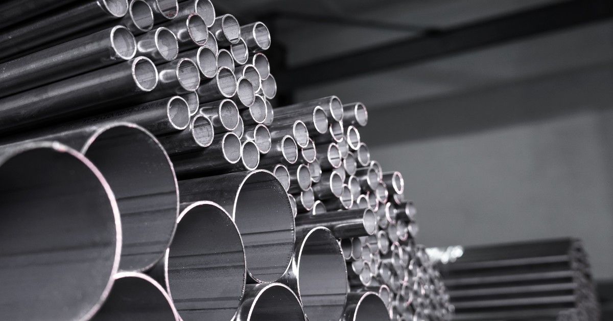Steel pipes of various diameters and lengths are stacked in organized rows inside a warehouse facili