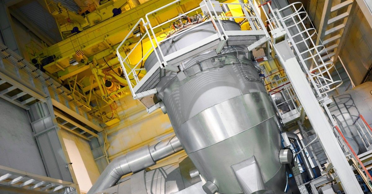 A large stainless steel industrial duct system features access stairs on the side and a platform run