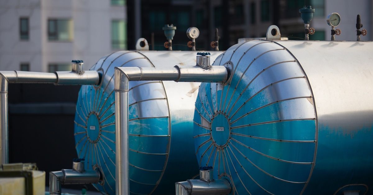 Two pressure vessels with gauges and connected pipes sit side by side on a rooftop in an urban envir