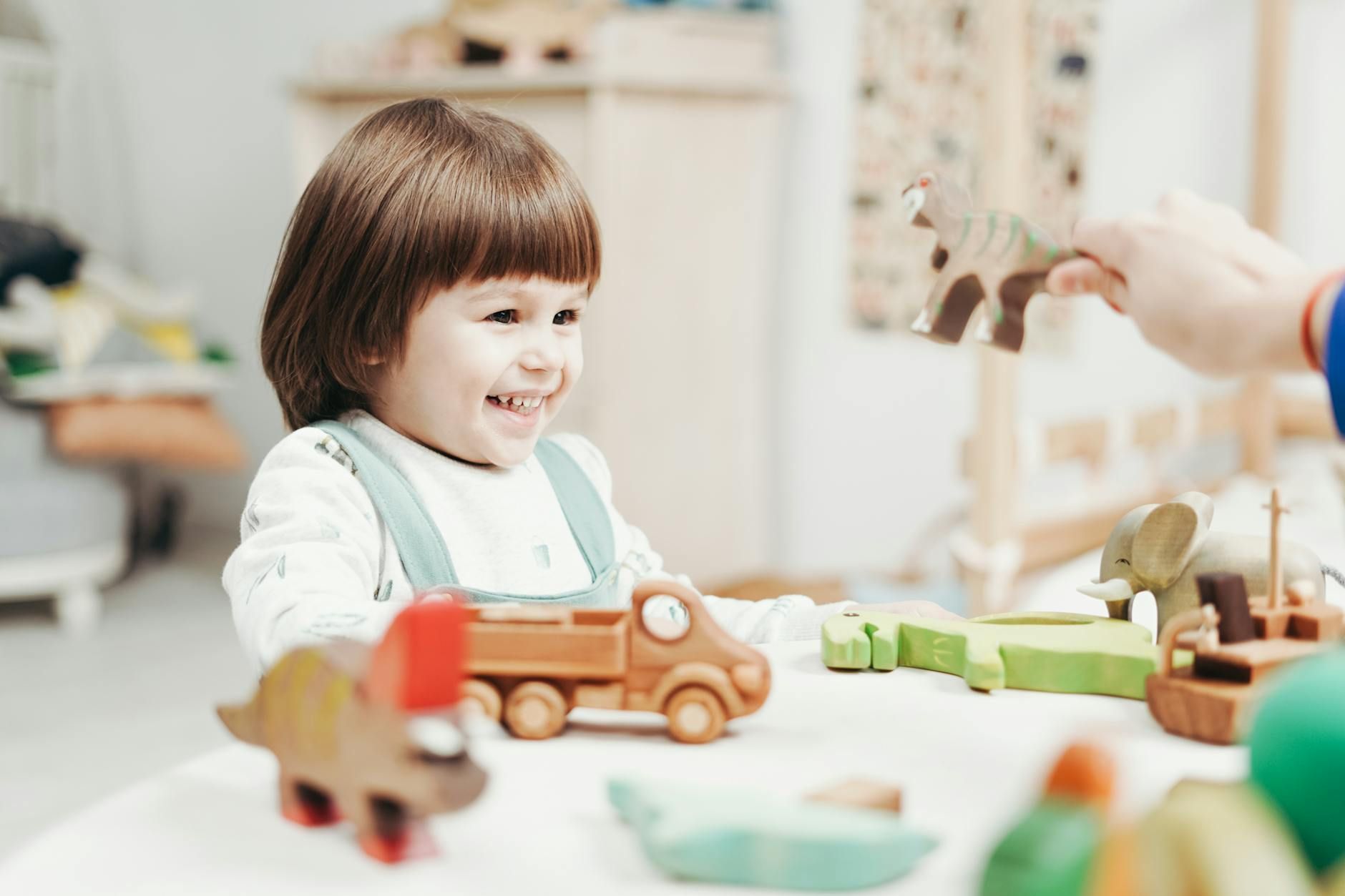 Smiling autistic toddler playing with wooden animal toys at a table during ABA therapy in Maryland.