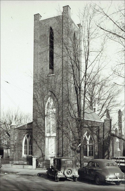 A black and white photo of a church with cars parked in front of it