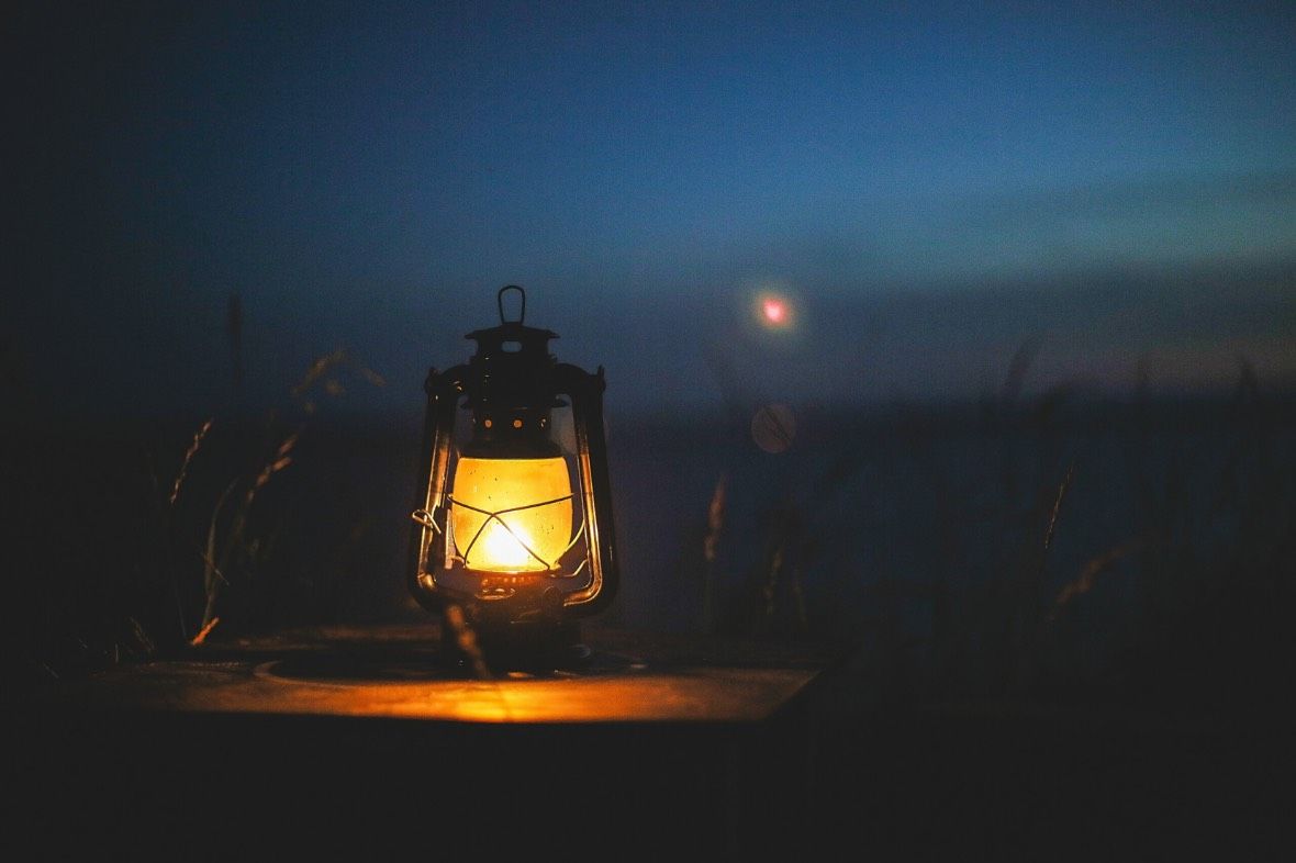 A lantern is lit up in the dark with a full moon in the background.