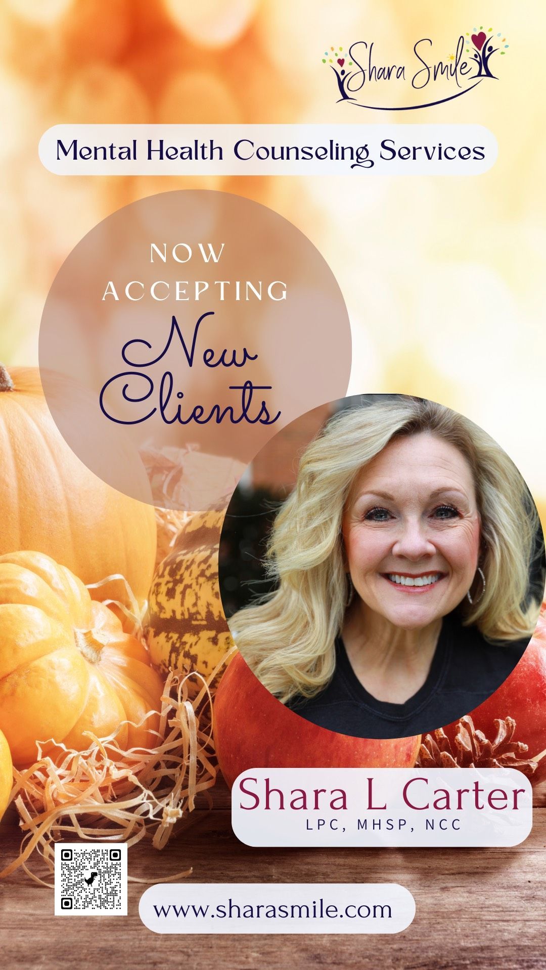 A woman is smiling in front of a pile of pumpkins.