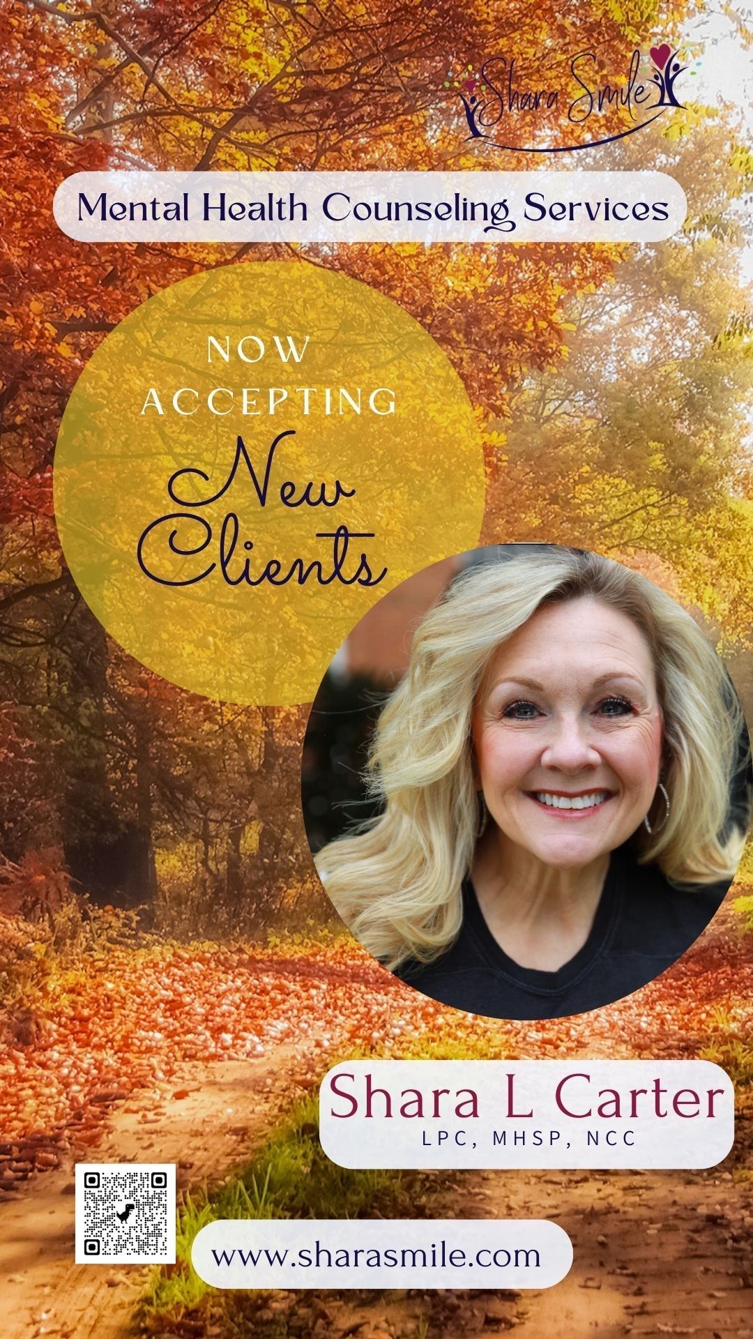 A woman is smiling in front of a forest with autumn leaves.