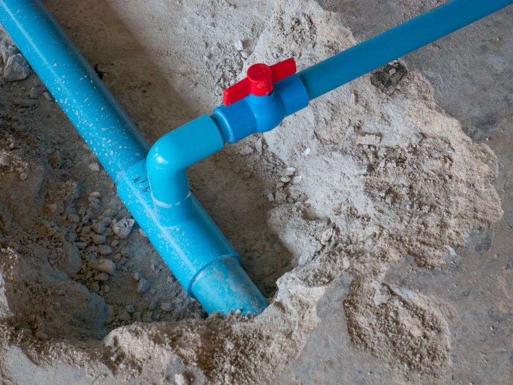 Blue PVC pipes with a red valve in a concrete trench.