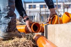 Person connecting orange drainage pipes near a concrete structure outdoors.