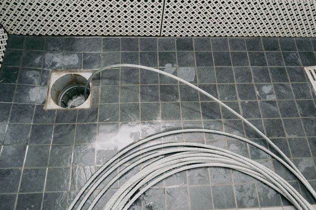 Gray cable extending from a drain on a tiled floor, coiling at the bottom.