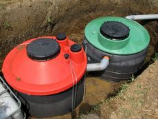 Two connected septic tanks, one red and one green, in a trench, with access covers.