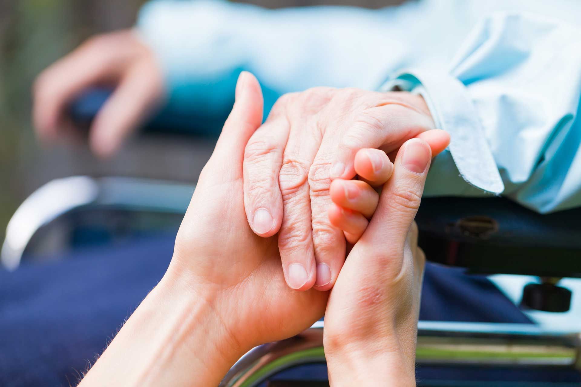 A woman is holding the hand of an elderly man in a wheelchair.
