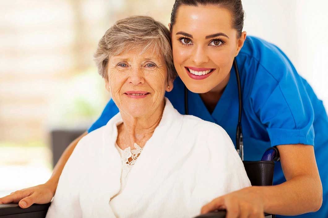 A nurse is standing next to an elderly woman in a wheelchair.