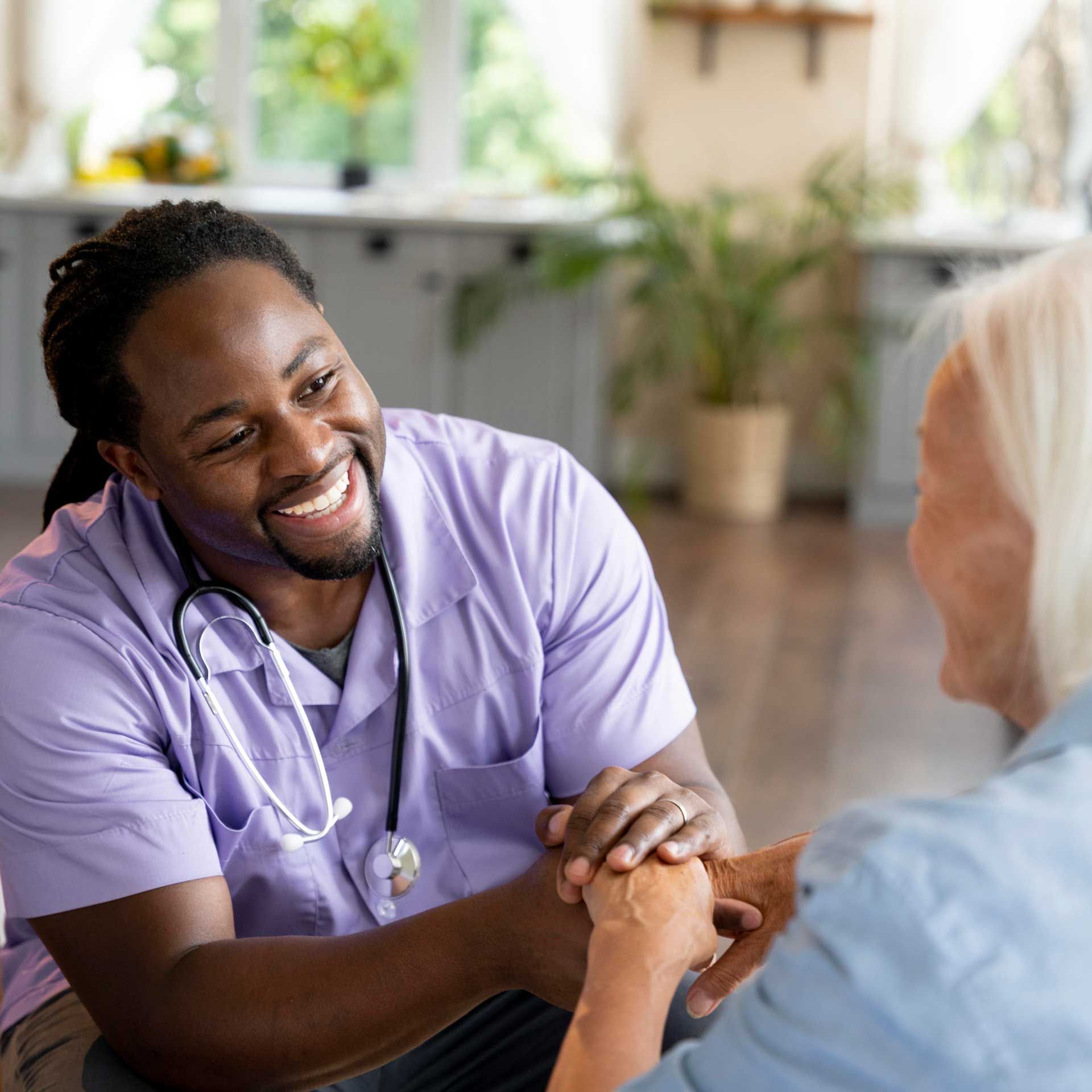 A nurse is holding the hands of an elderly woman and smiling.