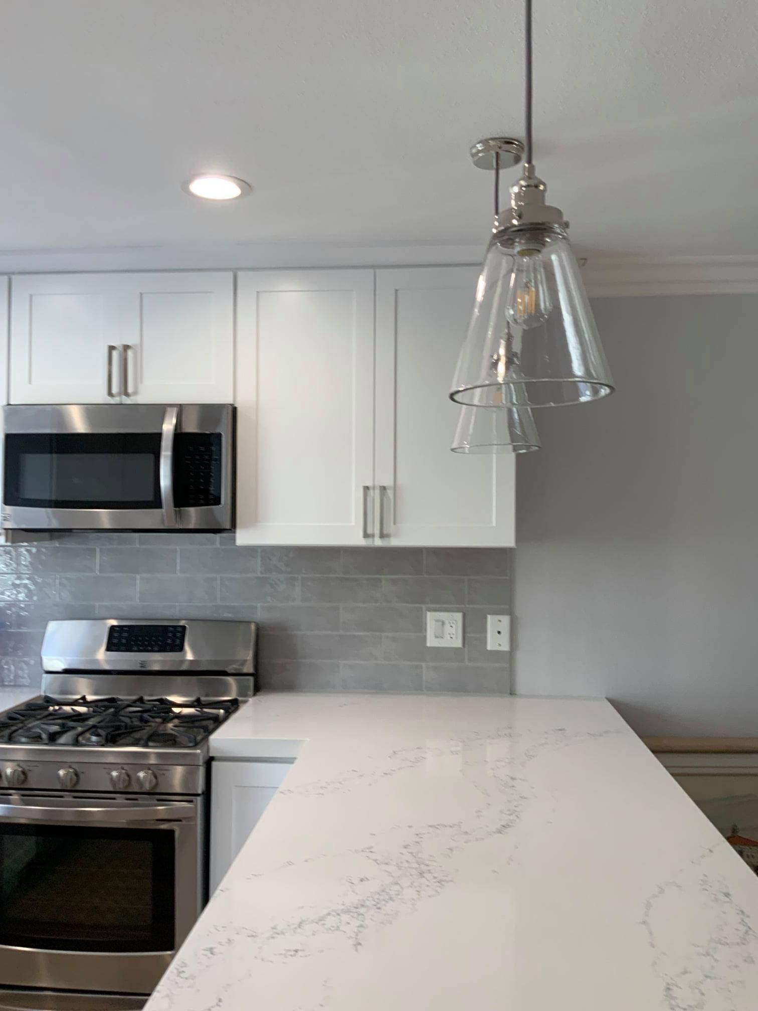 A kitchen with white cabinets , a stove , a microwave , and a pendant light.