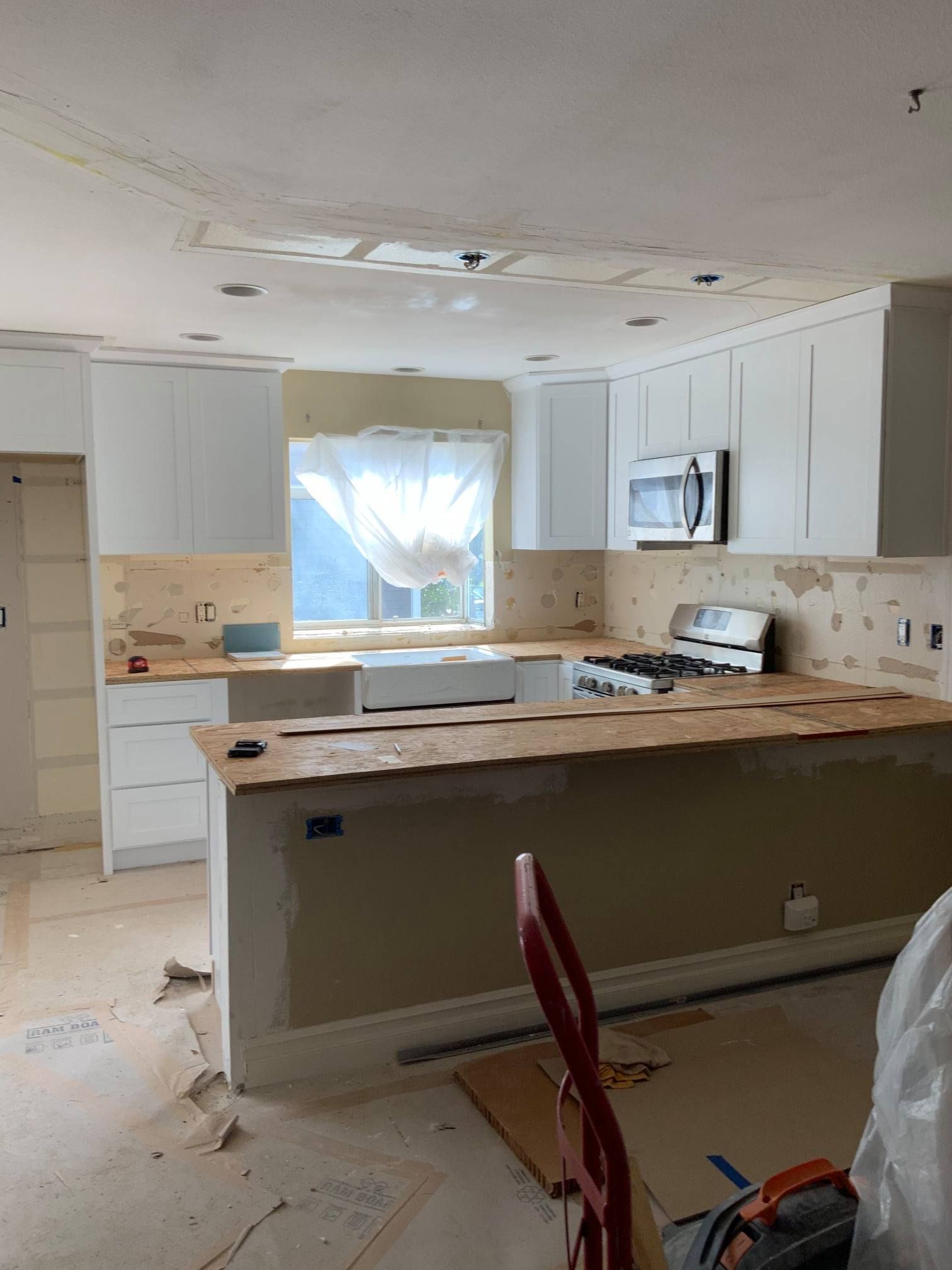 A kitchen under construction with white cabinets and a microwave.