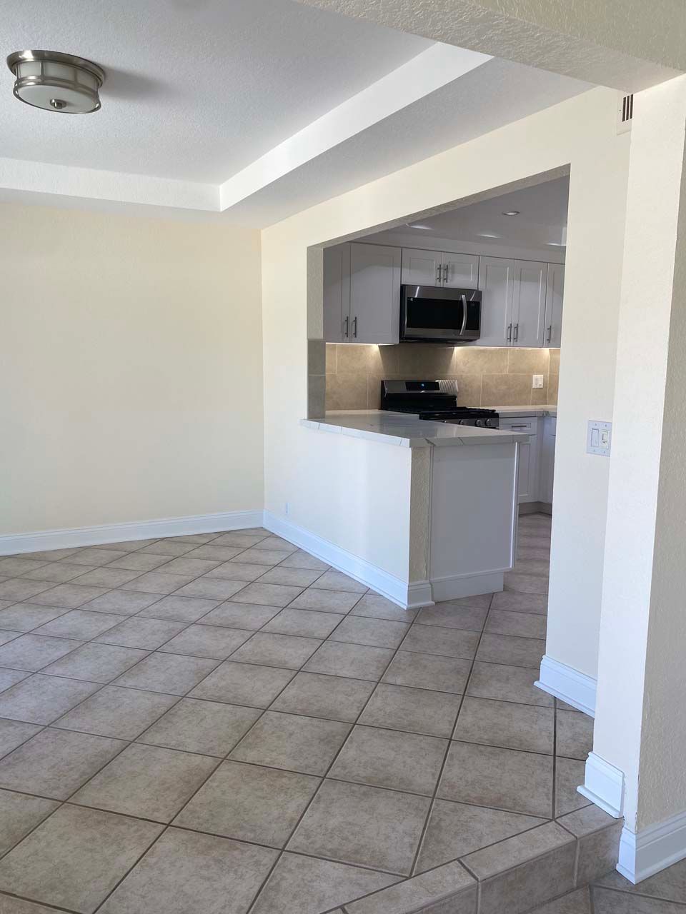 An empty room with a tiled floor and a kitchen in the background.