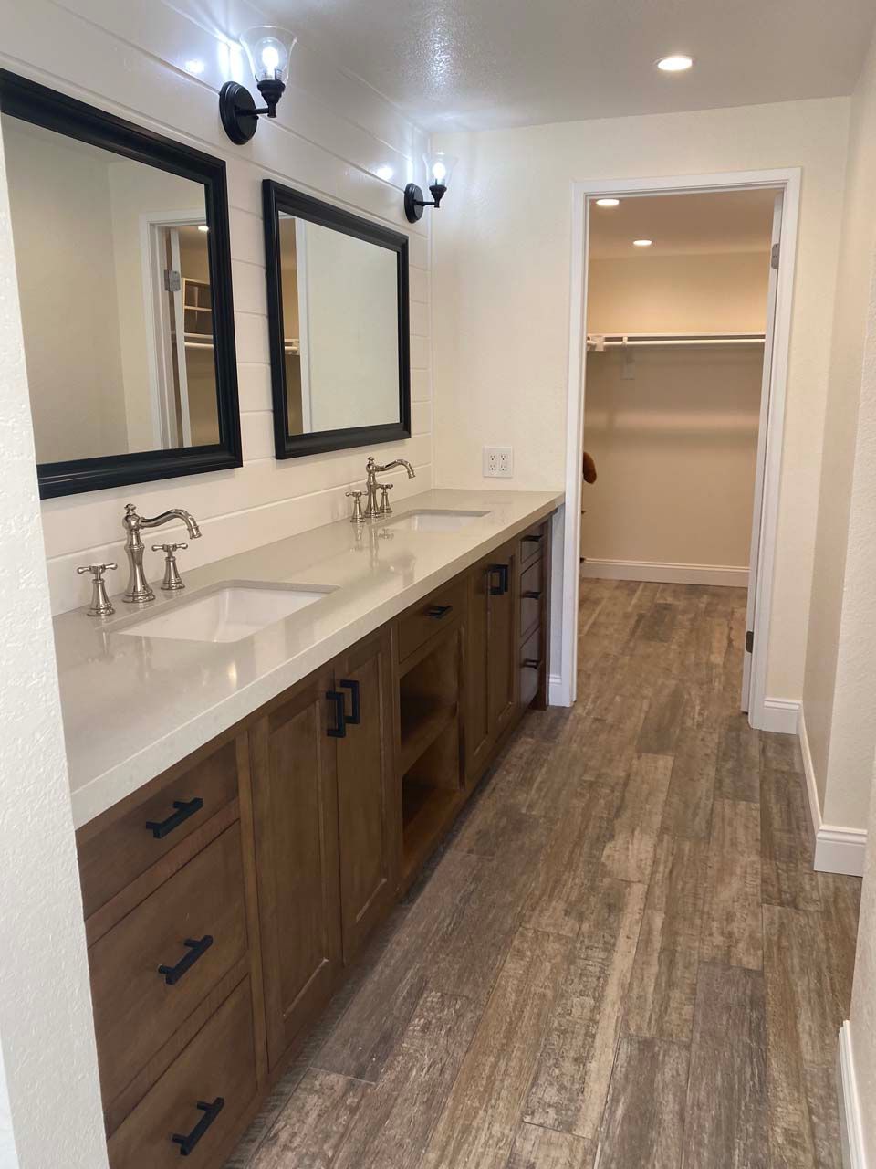 A bathroom with two sinks , two mirrors and a walk in closet.