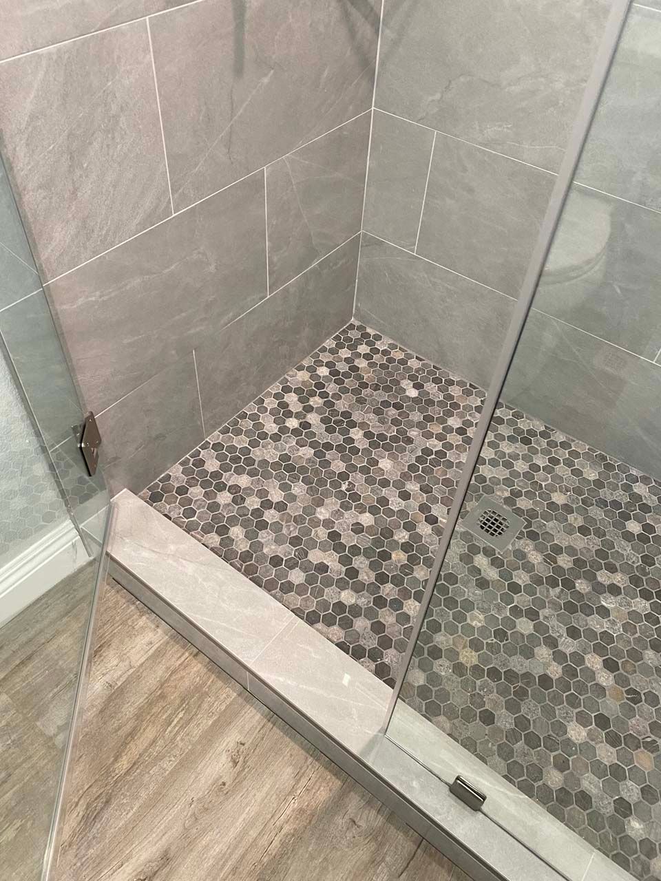 A walk in shower with a tiled floor and a glass door.