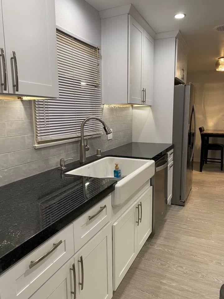 A kitchen with white cabinets , black counter tops , a sink and a refrigerator.