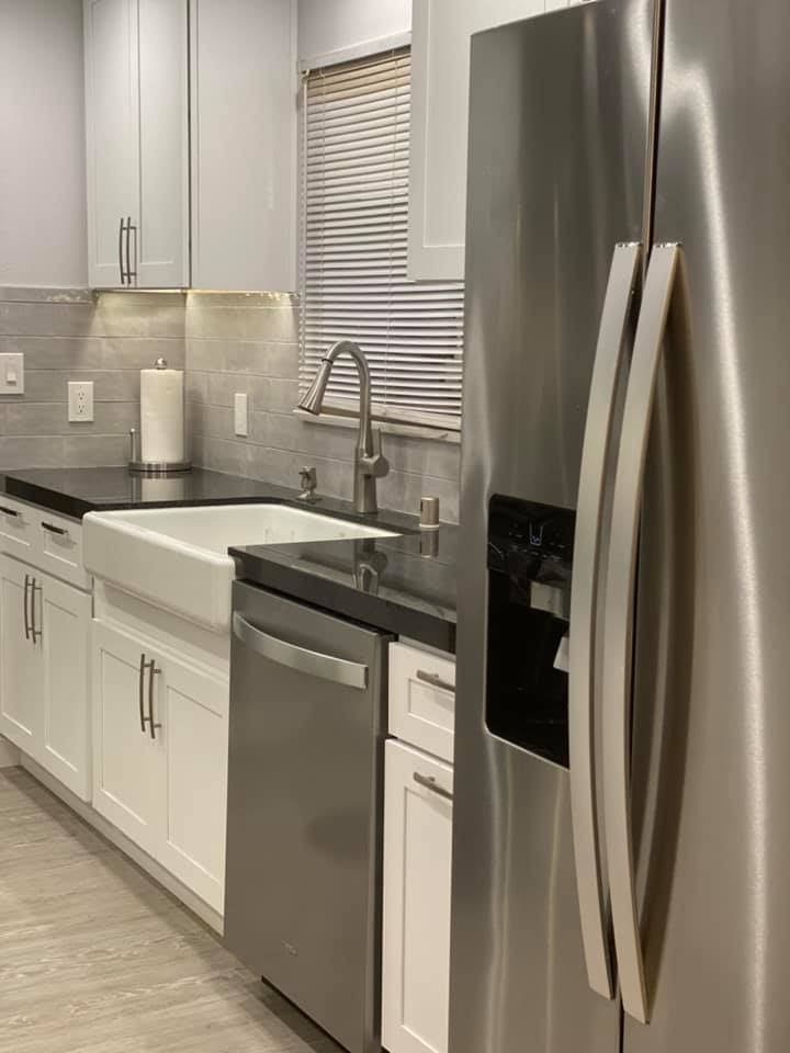 A kitchen with stainless steel appliances , white cabinets , a sink , and a refrigerator.
