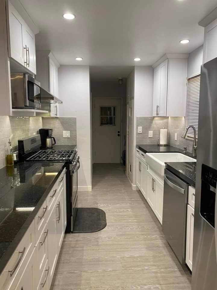 A kitchen with white cabinets , stainless steel appliances , a sink , and a refrigerator.
