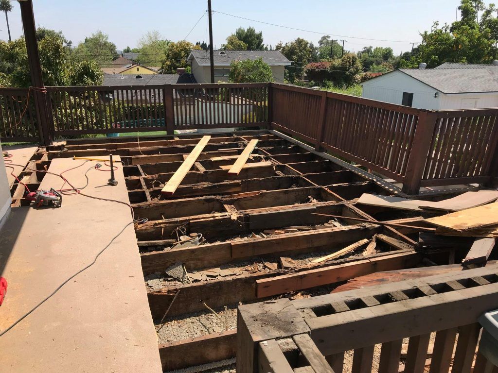 A wooden deck is being demolished with a fence in the background.