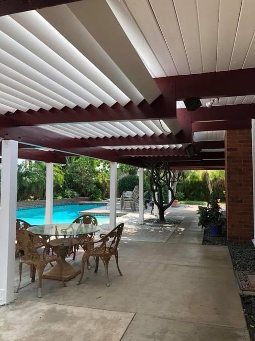 A patio with a table and chairs under a pergola next to a pool.