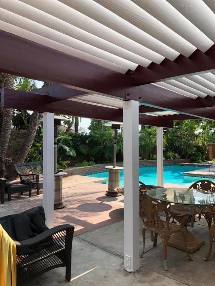 A patio with a table and chairs under a pergola next to a pool.