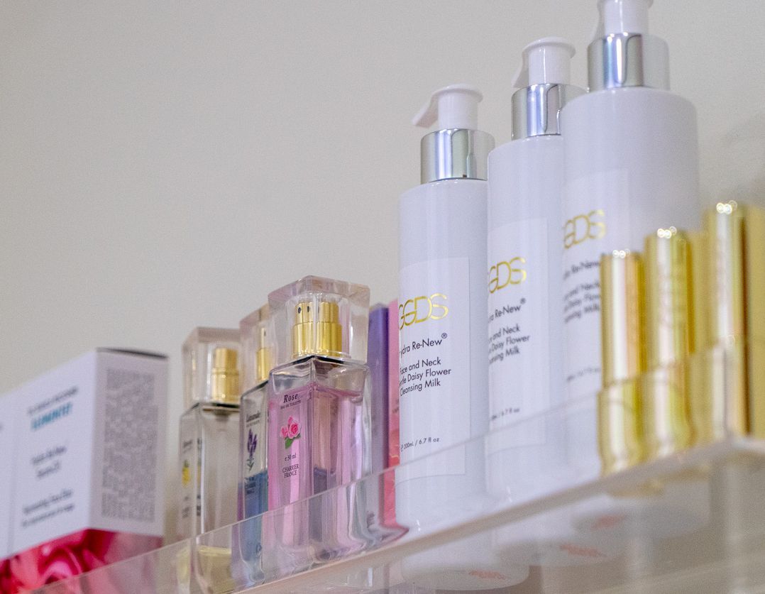 Clear plastic shelf holding various skincare bottles, including white pump dispensers, perfume, and gold-capped items.