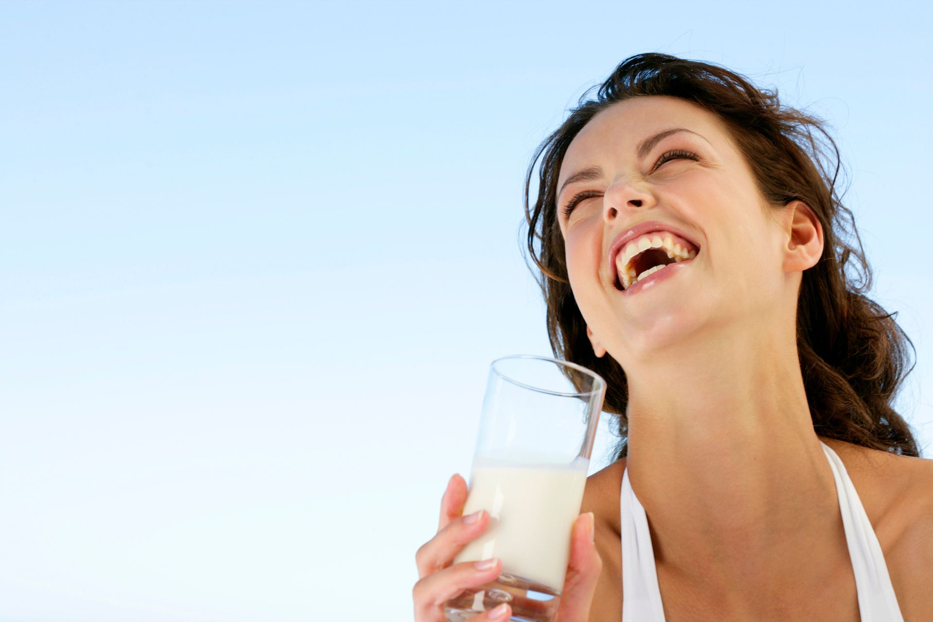 A woman is holding a glass of milk and laughing.