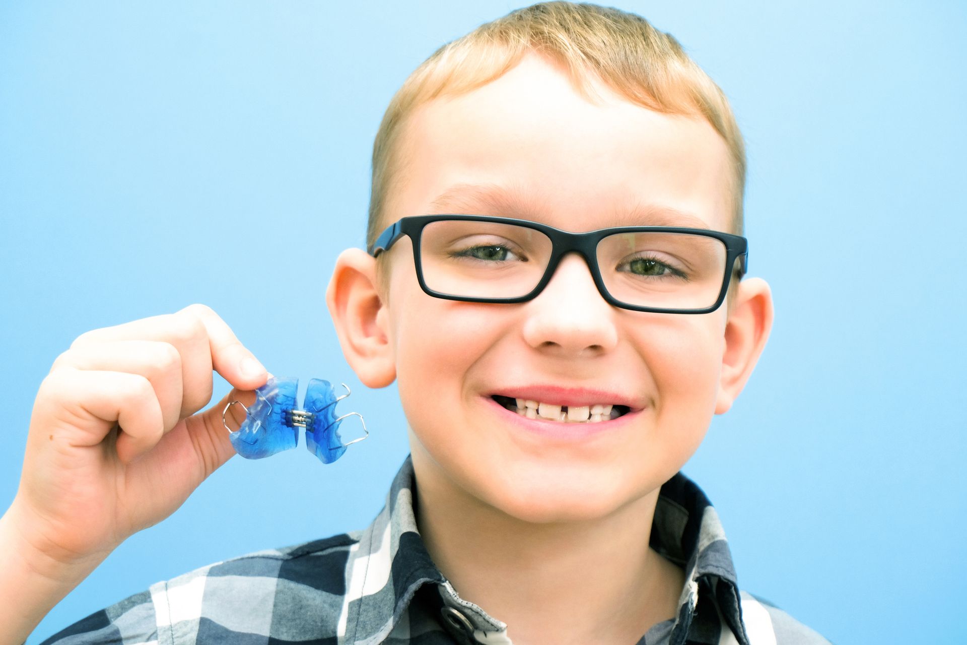 A young boy wearing glasses is holding a retainer in his hand.